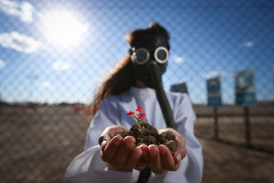 Girl wearing gas mask while holding flower plant