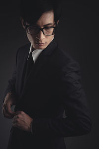 Young man looking away while standing against black background