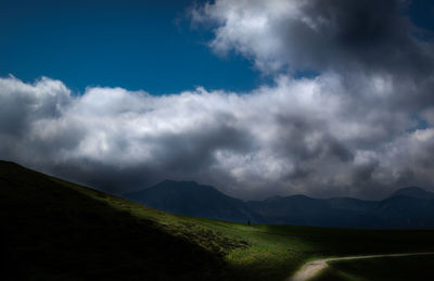 Grassy hills crossed by a path, mountain profiles and blue sky with stormy clouds. high contrast