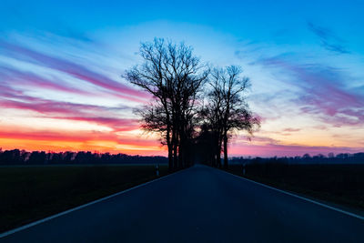 Silhouette tree by road against sky during sunset