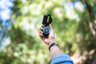 Cropped hand holding navigation compass against trees