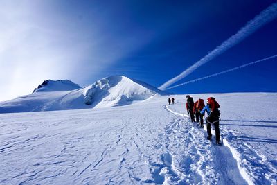 People hiking on snow covered land against sky