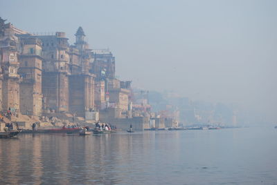Temple by ganges river against sky in foggy weather