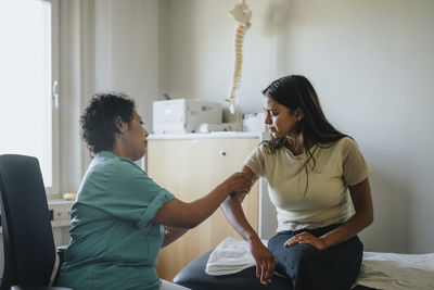 Side view of female doctor examining arm of young woman during medical