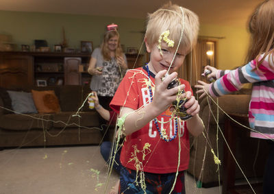 Boy holding party spray during celebration in living room at home 
