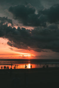 Silhouette people on beach against sky during sunset