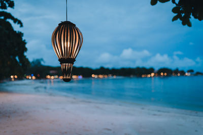 Illuminated electric lamp by sea against sky