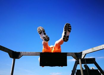 Low angle view of boy swinging against blue sky