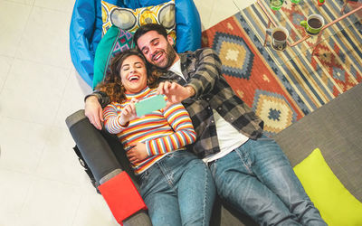 High angle view of cheerful couple taking selfie with smart phone while lying on sofa