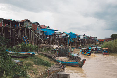 Boats moored on beach by houses against sky