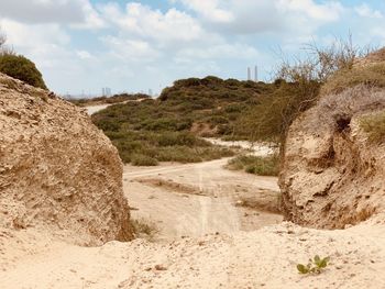 Dirt road amidst rocks on field against sky