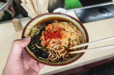 Close-up of human hand holding noodle soup in bowl