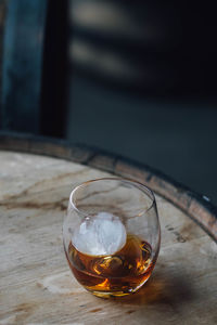 Close-up of whiskey in glass with ice sphere on bourbon barrel 