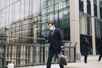 Male entrepreneur text messaging through smart phone while walking on bridge during pandemic