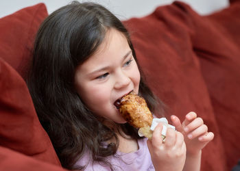 Expressive young girl is eating chicken and vegetables for dinner on the couch while watching tv