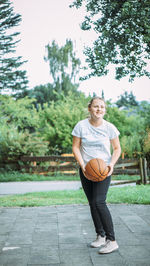 Young woman playing basketball while standing on field