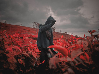 Man standing by red umbrella against sky during autumn