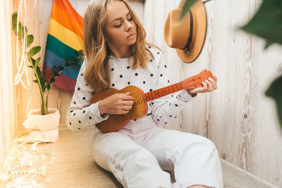 Young millennial hippie woman sitting on balcony play guitar. music lesson and singer sitting. lgbtq 