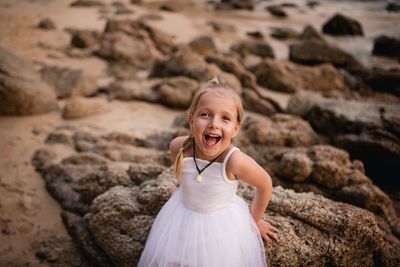 Portrait of happy girl sitting on rock at beach