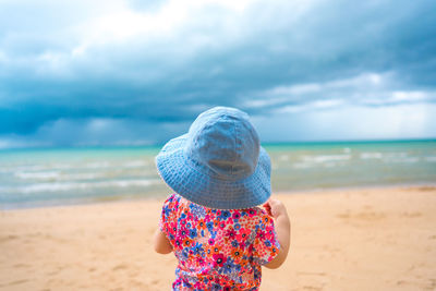 Rear view of girl wearing sun hat at beach against sky