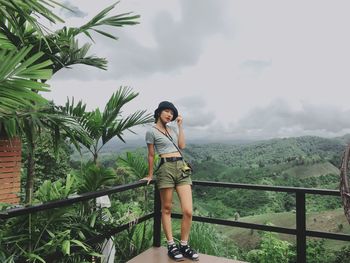 Young woman standing by railing against sky