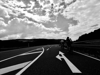 Men riding motorcycle on road against cloudy sky