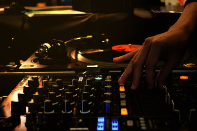 Cropped hand of dj using sound mixer in nightclub at night