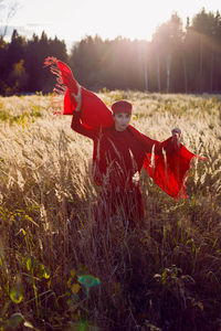 Woman in a red sweater cap and scarf stands in a field in autumn in the tall dry grass