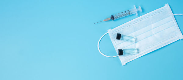 High angle view of syringe and mask on blue background