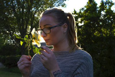 Woman smelling rose while standing in backyard