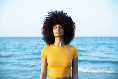 Young afro woman with eyes closed standing at beach