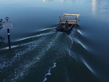 Rear view of man carrying wooden table on motorboat in water