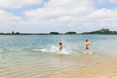 Boys with water wings running at beach against sky