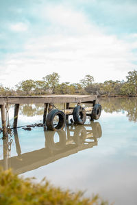 Pier with reflection of trees on river against sky