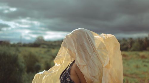 Side view of woman with fabric covering face against cloudy sky