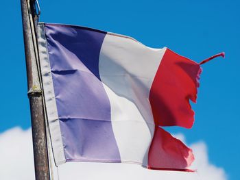 Low angle view of torn french flag against blue sky