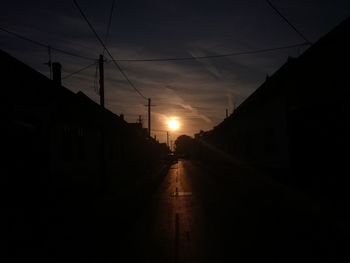 Road amidst silhouette buildings against sky during sunset