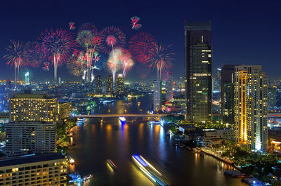 Illuminated modern buildings by river against sky at night