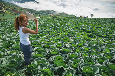 Portrait of smiling woman with book standing amidst vegetables on farm