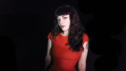 Portrait of young woman wearing make-up and red dress against black background