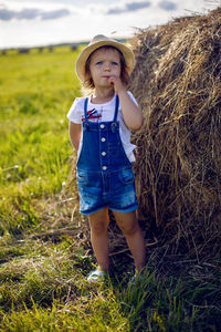 Little girl in the haystack in a hat and denim overalls