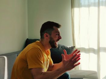 Side view of man screaming while sitting at home