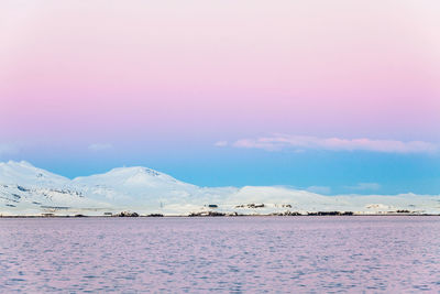 Scenic view of lake by snowcapped mountains against sky during sunset