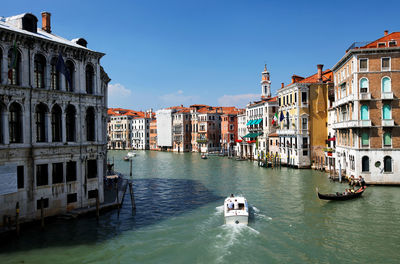 Gondolas moving on grand canal amidst buildings against clear blue sky