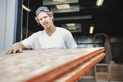 Portrait of confident carpenter carrying wooden planks at workshop