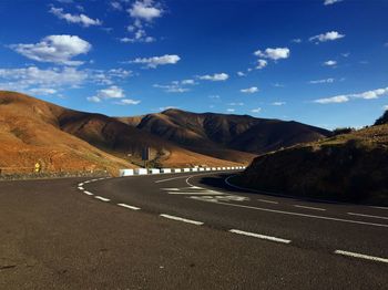 Empty road by mountains against sky