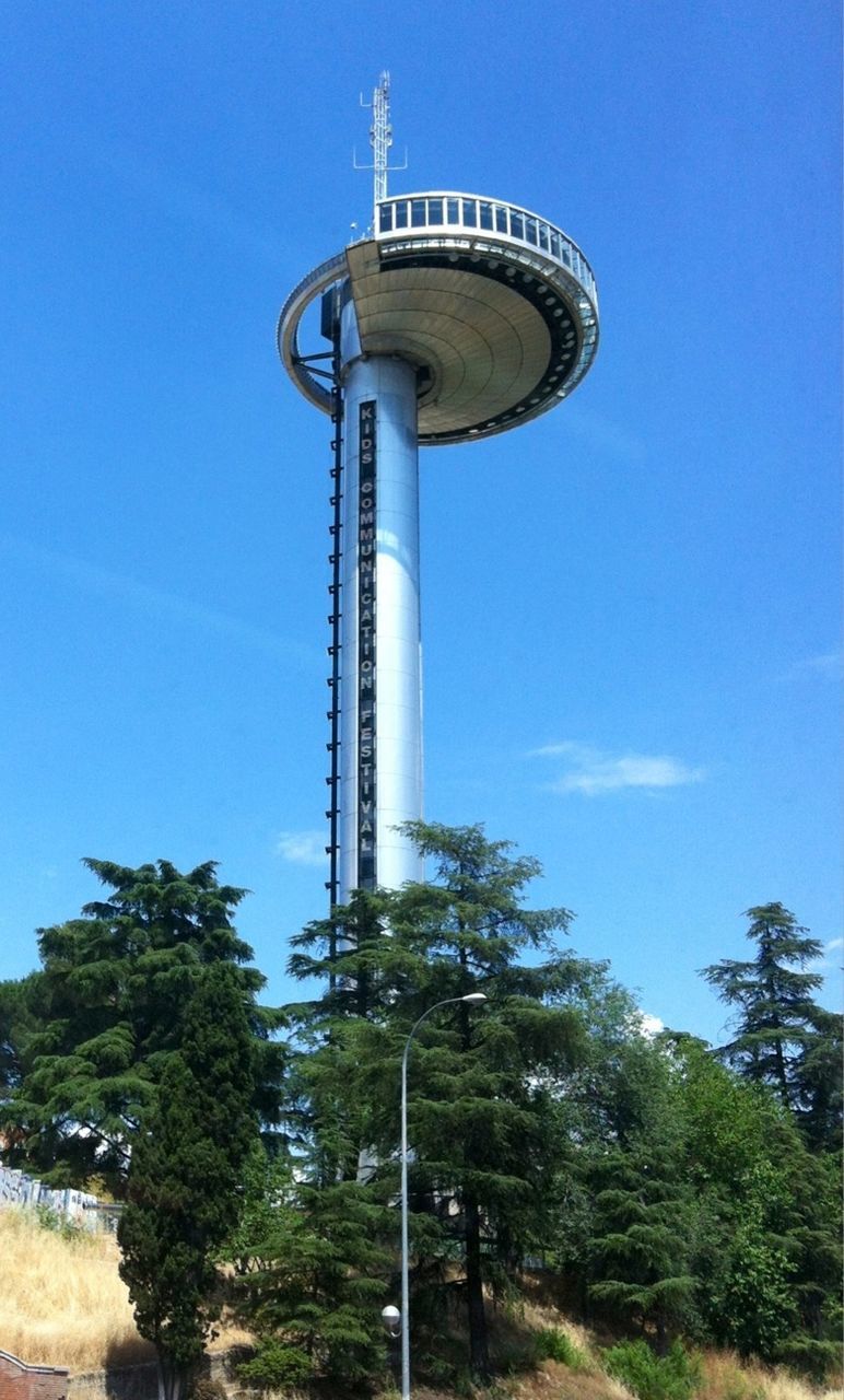 low angle view, blue, tower, tree, built structure, architecture, tall - high, communications tower, clear sky, sky, building exterior, street light, day, travel destinations, outdoors, technology, no people, growth, communication, lighting equipment