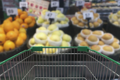 Close-up of shopping cart against fruits for sale in store