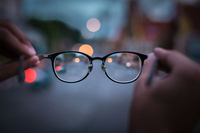 Cropped hands of person holding eyeglasses during sunset