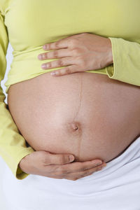 Close-up of pregnant woman touching belly against white background